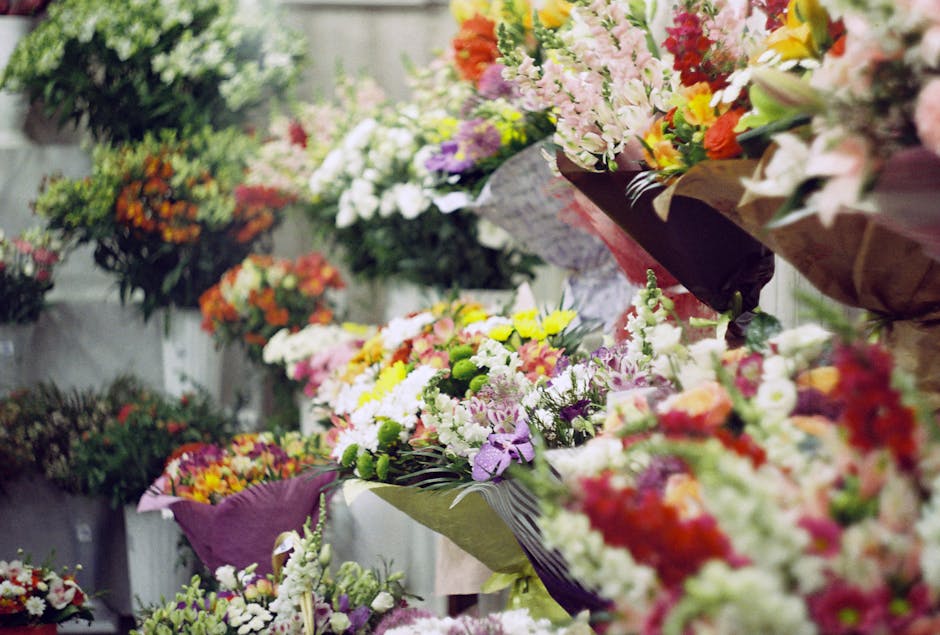 A wide view of a flower shop display featuring an assortment of fresh floral arrangements and bouquets. The flowers include pink, yellow, purple, white, and orange blooms, with varieties such as lilie